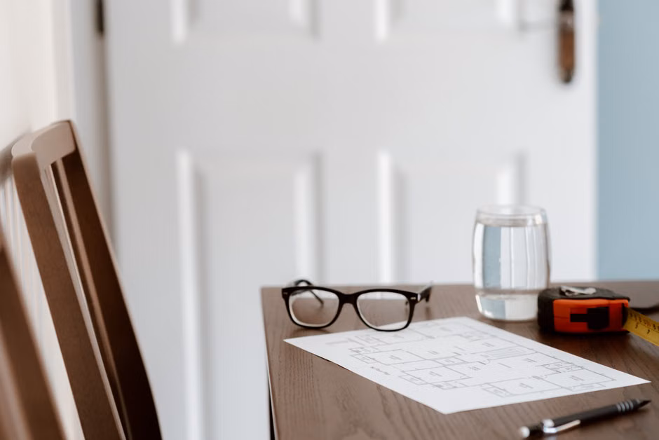 Um escritório em casa contemporâneo com plantas, óculos e uma fita métrica sobre uma mesa de madeira.